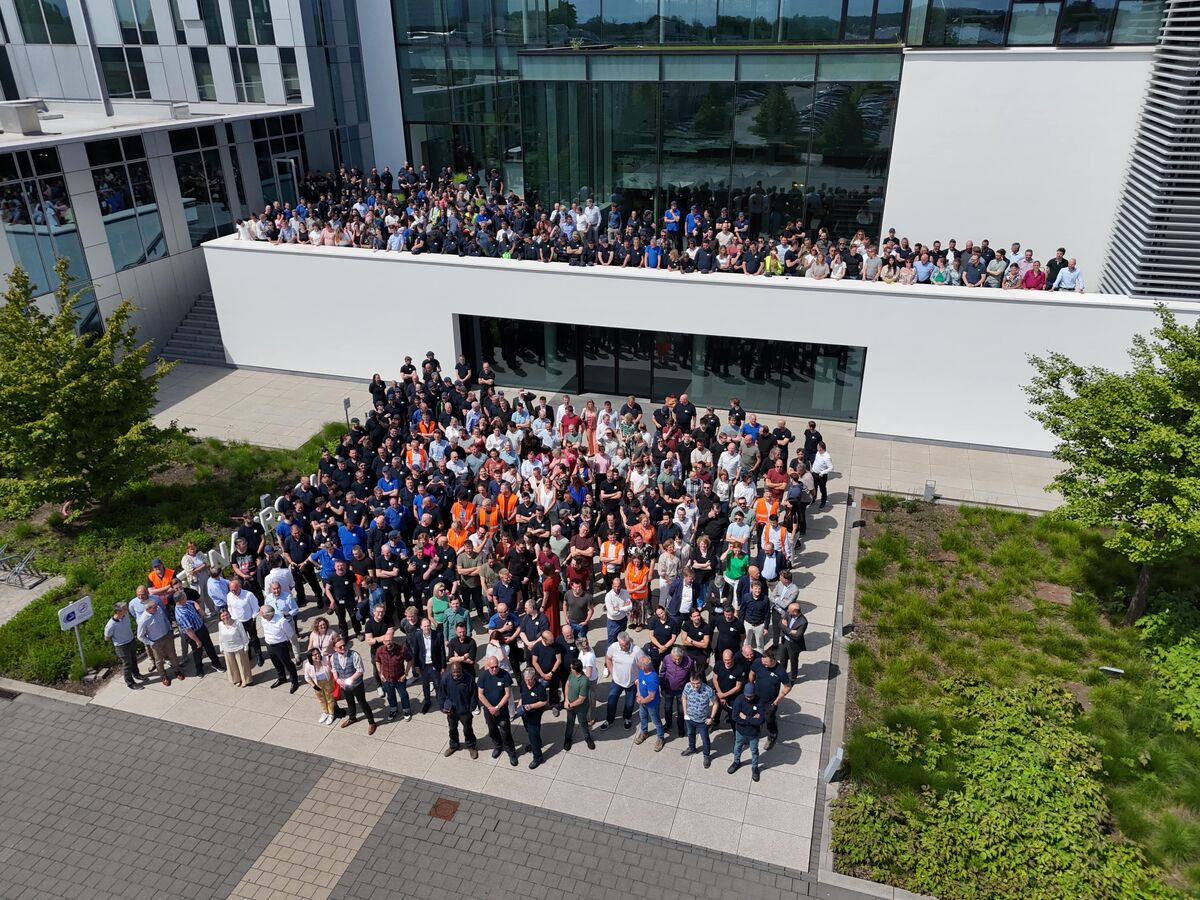 Групова фотографія співробітників на фоні Reynaers Campus.