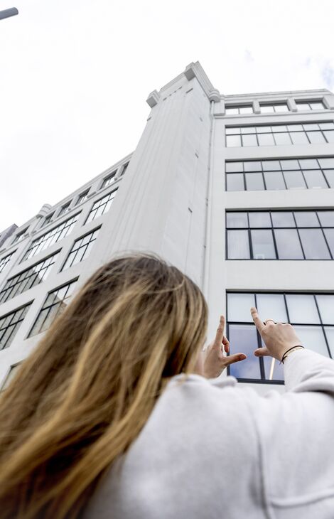 Жінка дивиться та вказує на середньоповерхову білу офісну будівлю в Нідерландах.