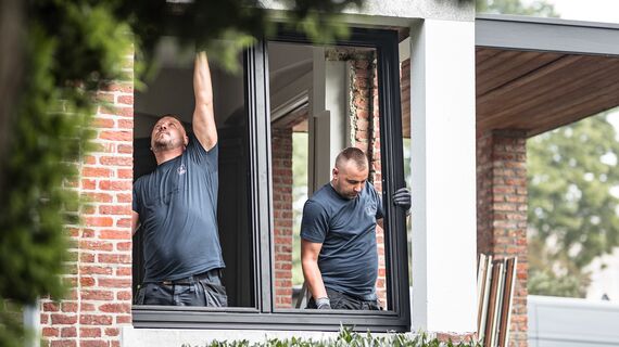 Два монтажники встановлюють нові алюмінієві профілі у відремонтованому будинку.
